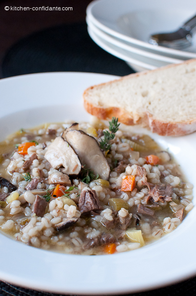 White bowl full of soup. A piece of french bread sits on the side, and in the background are more empty bowls and spoons.