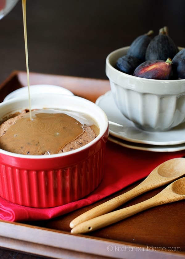 A red dish full of Sticky Toffee Pudding Cake with Figs sitting beside a white bowl full of fresh figs.