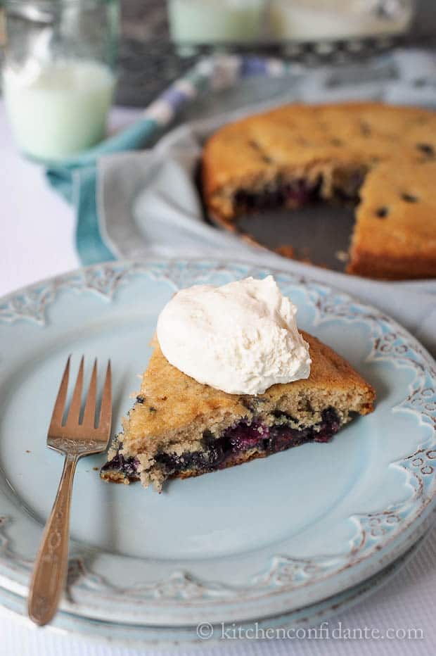 Slice of blueberry cake with whipped cream on blue plate.