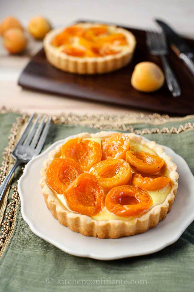 A perfectly fresh apricot tart sits on a white plate with a fork.