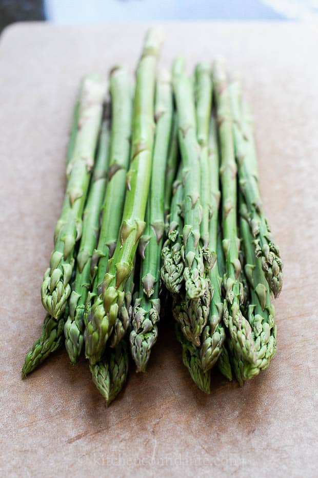 A pound of fresh asparagus lies on a wooden cutting board.