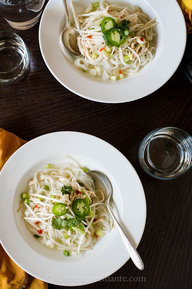 Two bowls of chicken pho topped with cilantro and jalapeno slices.