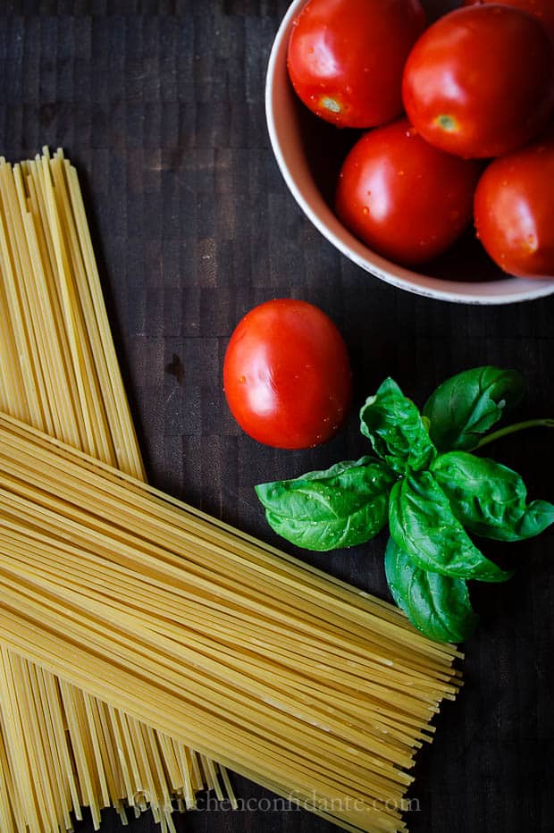 Uncooked dried spaghetti, basil leaves, and whole roma tomatoes.