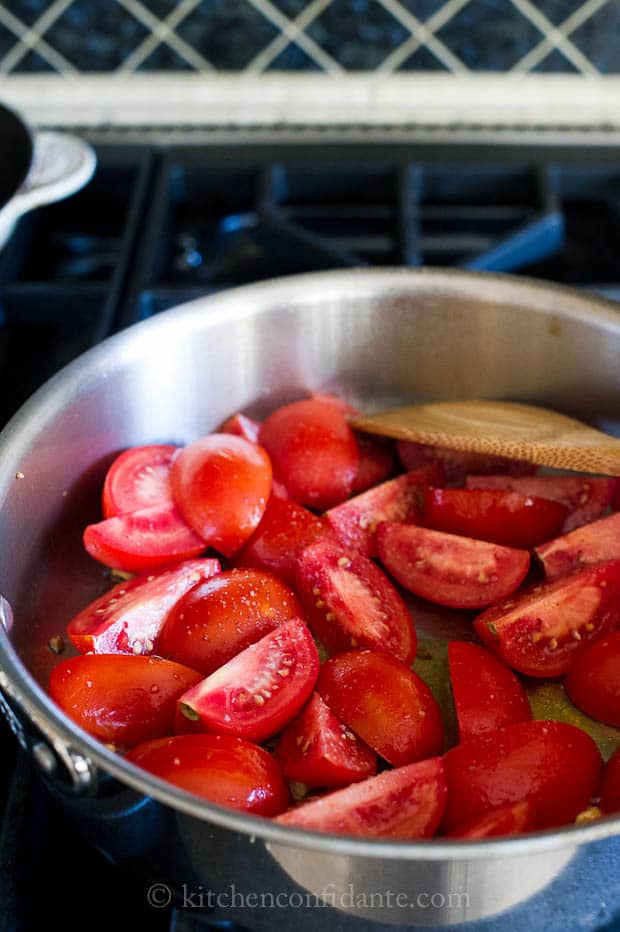 A saute pan full of quarered tomat tomatoes.