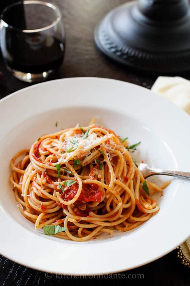 A white bowl filled with spaghetti made with homemade spaghetti sauce topped with fresh basil and parmesean reggiano cheese.