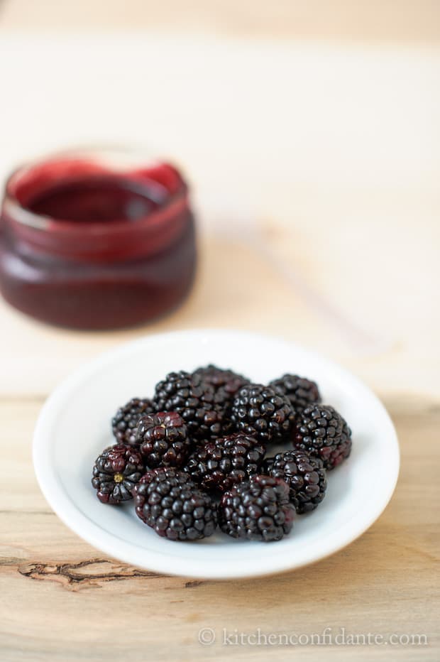 A dish of blackberries sits in front of a jar of glaze for blackberry ribs.