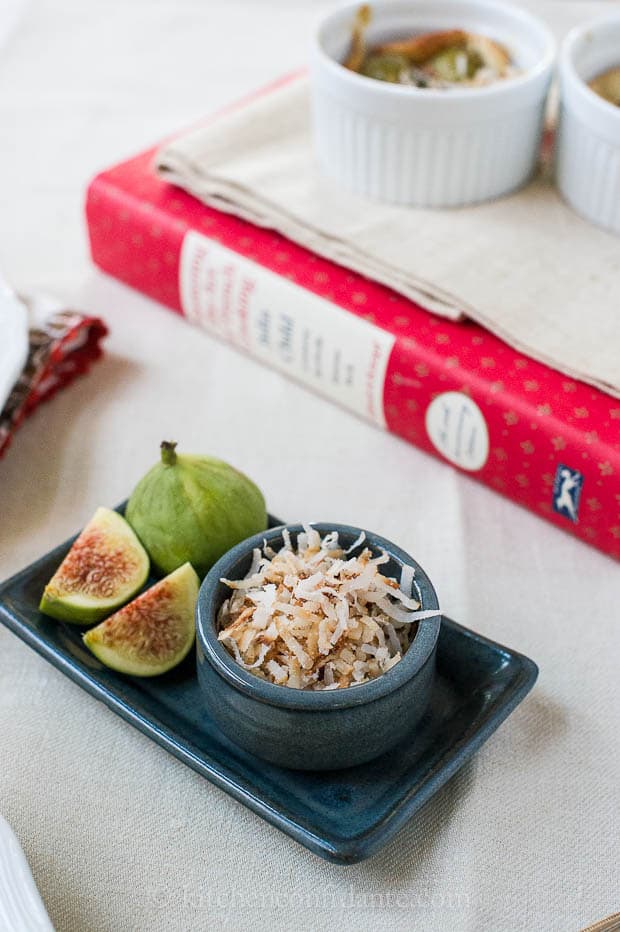 A small blue rectangular dish has fresh fig slices, and a smaller blue dish full of toasted coconut.