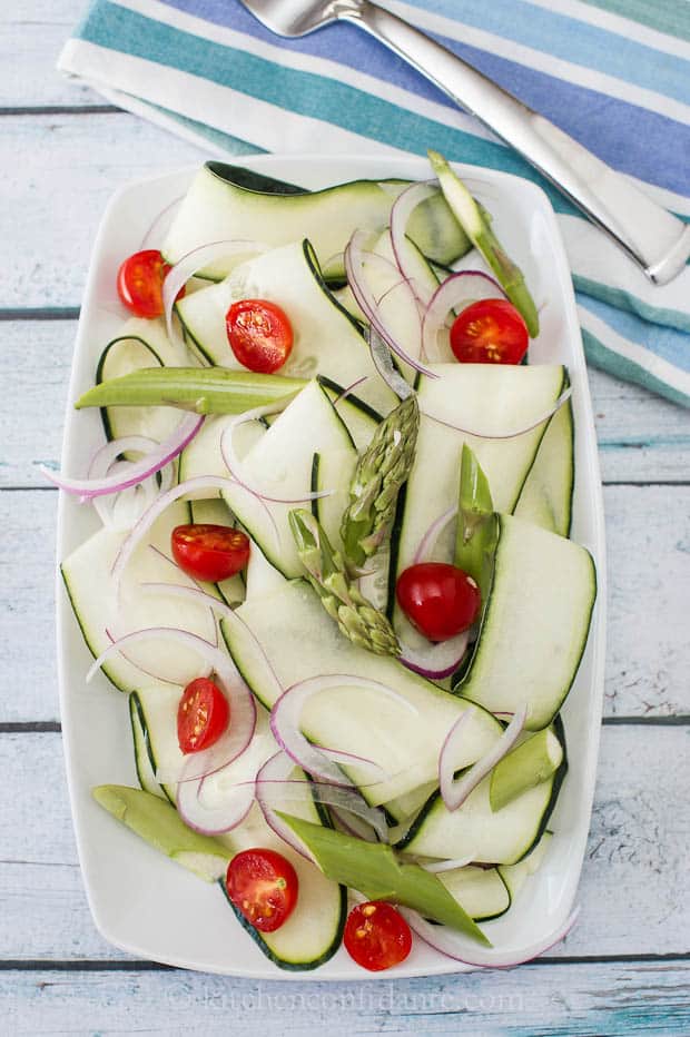 A sliced cucumber salad lies in a white dish on a blue striped towel.