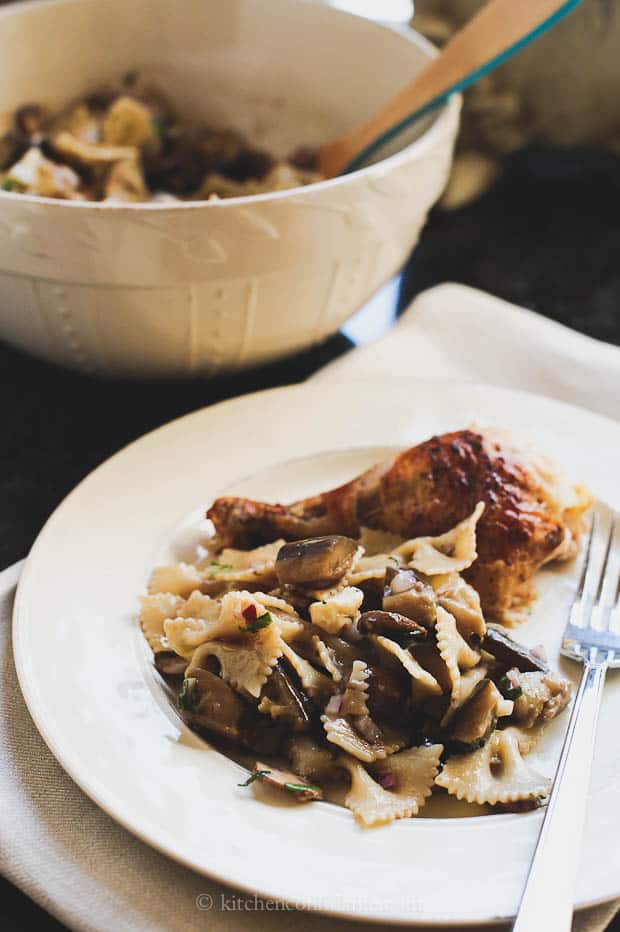 A plate of eggplant mushroom pasta next to a chicken leg.