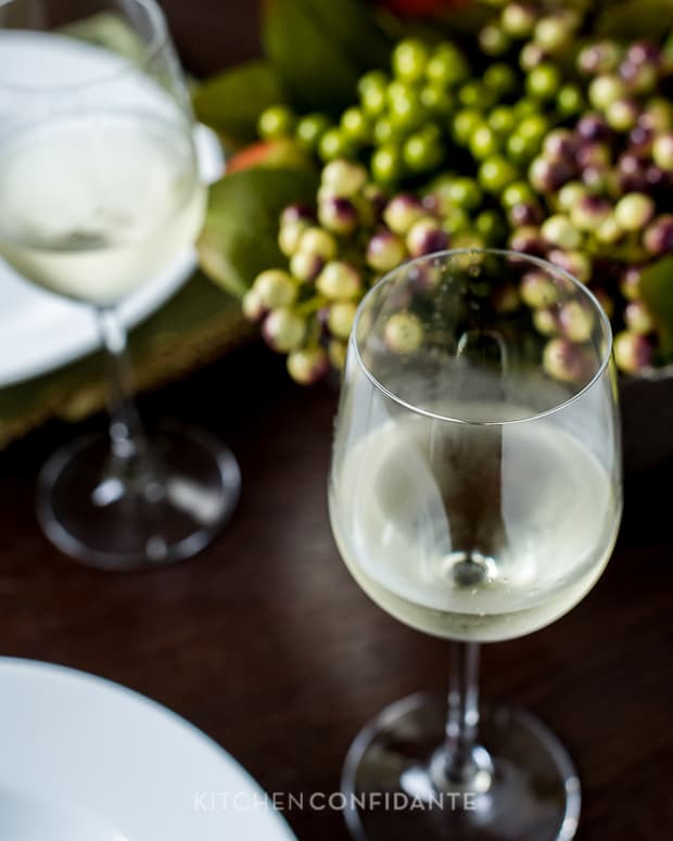 A glass of white wine. Some green and purple grapes are in the background.