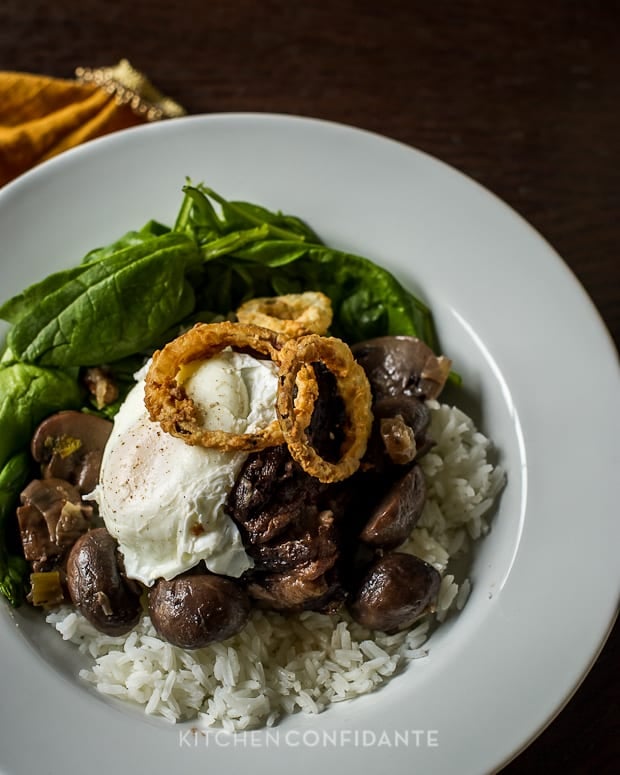 A white dish of short ribs loco moco on rice in a white dish.