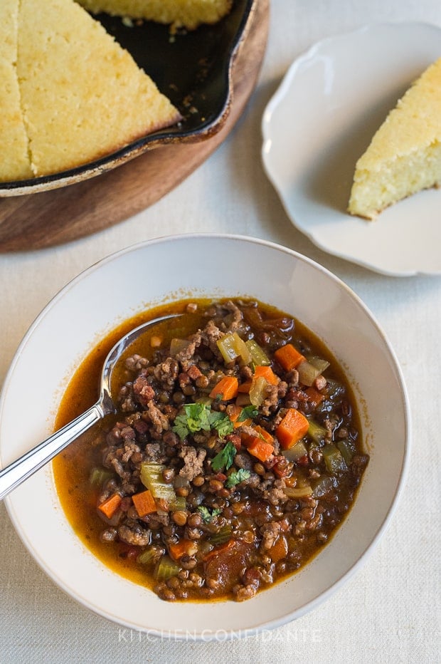 A bowl of beef and lentil chili and slices of cornbread.
