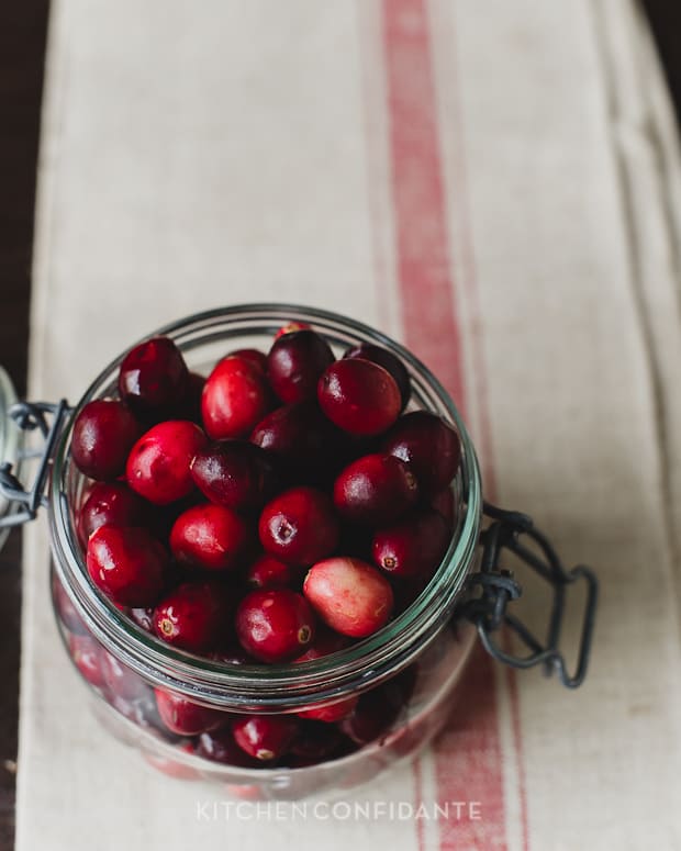 A glass jar filled with fresh cranberries.