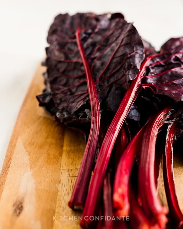 Stalks of red chard on a wooden cutting board.