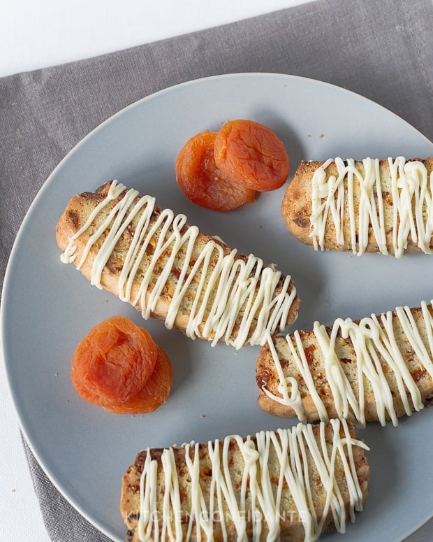 Apricot-White Chocolate Biscotti drizzled with chocolate and dried apricots on a plate.