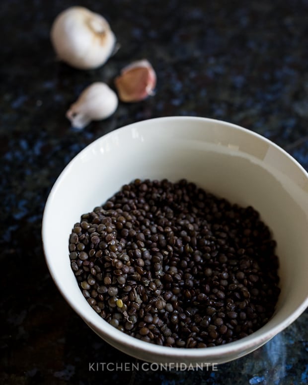 Black Beluga Lentils in a white bowl with cloves of garlic in the background.