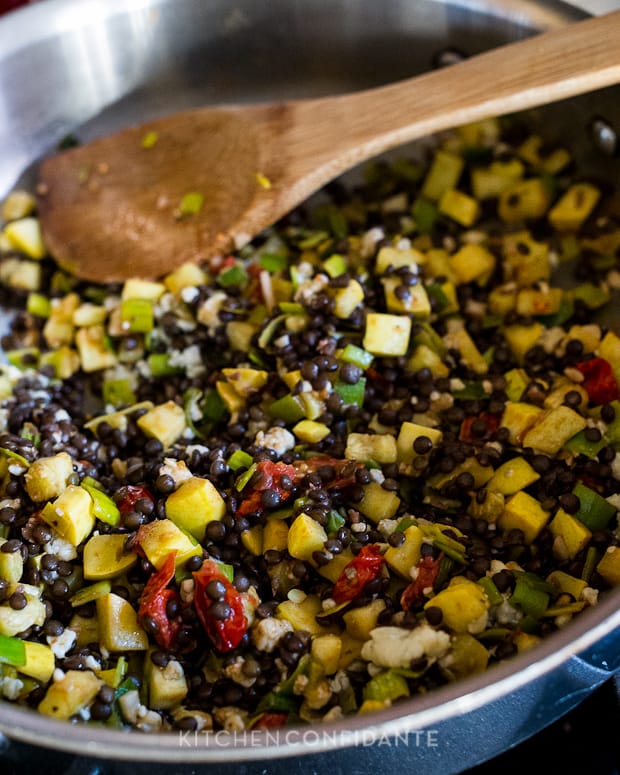 Cooking chopped yellow squash, chopped leeks, and black Beluga lentils in a pan on the stove.