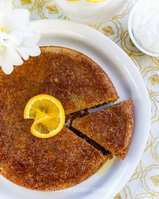 A one-layer Moroccan Orange Cake served on a white platter with a slice slightly removed and an orange slice in the middle of the cake.