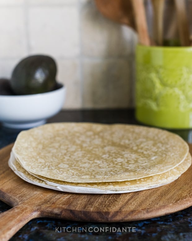 A wooden cutting board with a stack of whole grain tortillas.