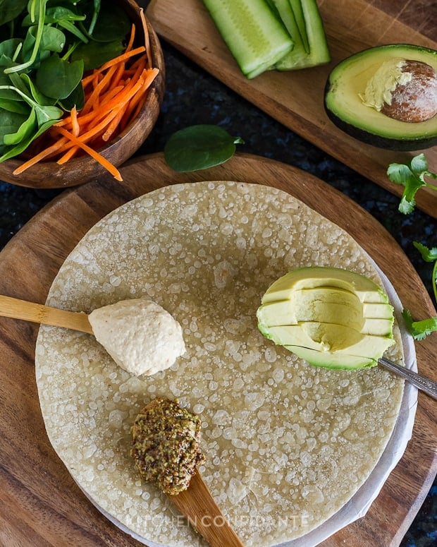 Whole grain tortilla with sliced avocado and spoonfuls of hummus and whole grain mustard.