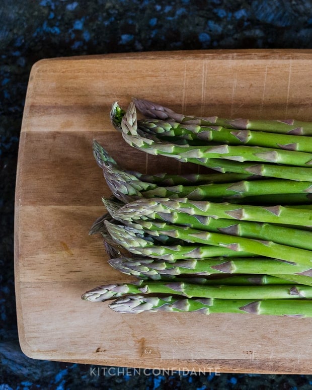 Stalks of asparagus on a wooden cutting board.