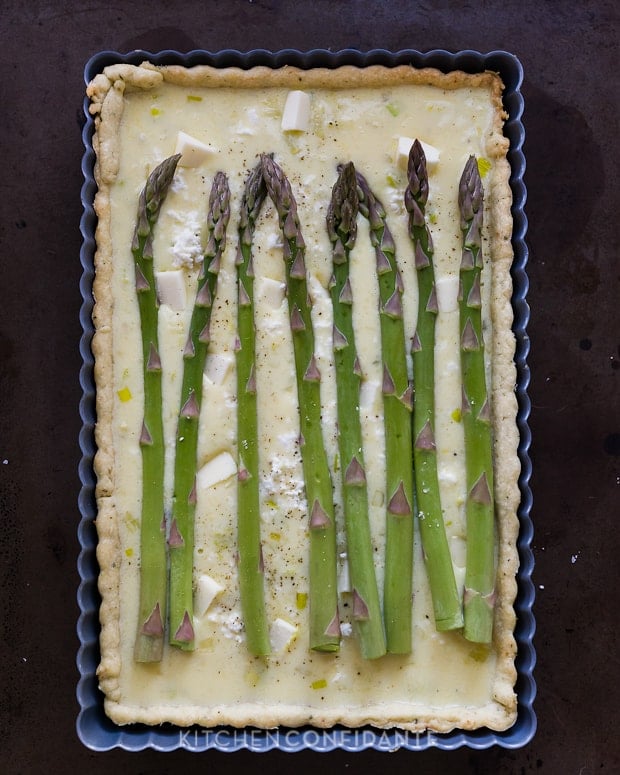 A rectangle tart pan filled with crust, custard, and asparagus, ready to bake.