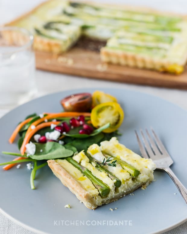 A slice of Buttermilk Asparagus Quiche on a gray-blue plate with a side salad.