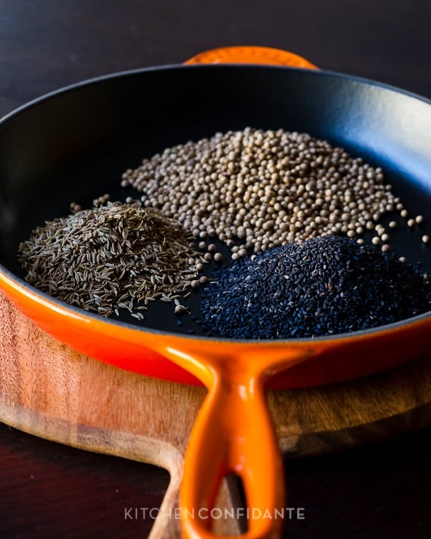 Sesame, cumin, and coriander seeds toasting in a cast iron pan.