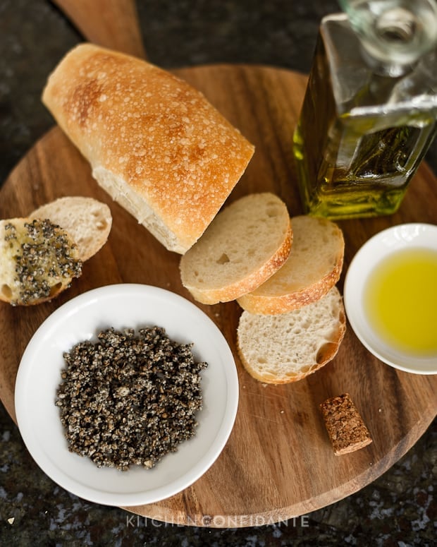 A bowl of Macadamia Nut Dukkah, a loaf of sliced bread and a small dish of olive oil.