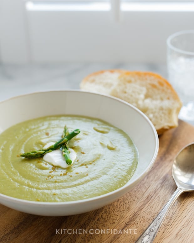 A bowl of green roasted asparagus soup garnished with asparagus tips and crème fraiche. 