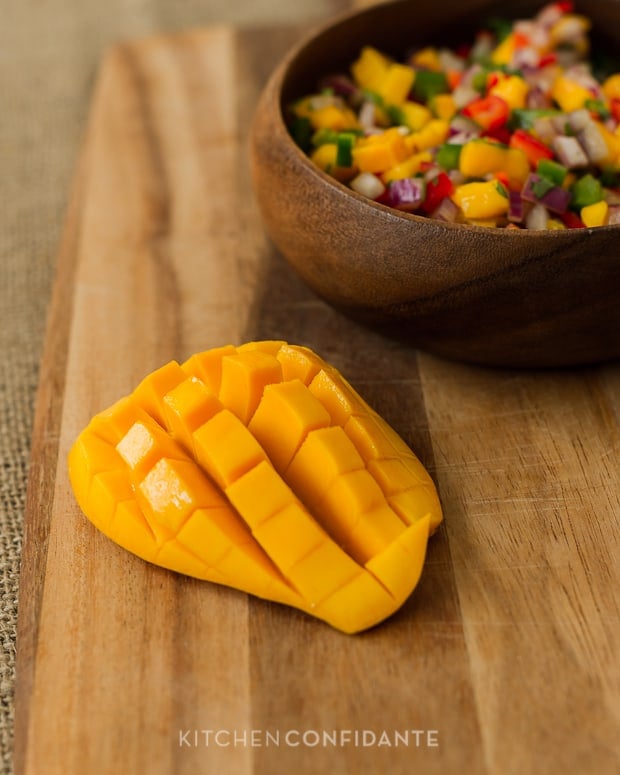 Half of a sliced mango with a bowl of fresh salsa in the background.