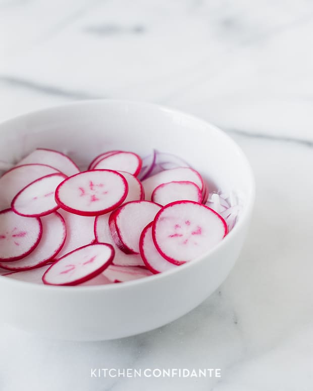 A white bowl of sliced radishes.