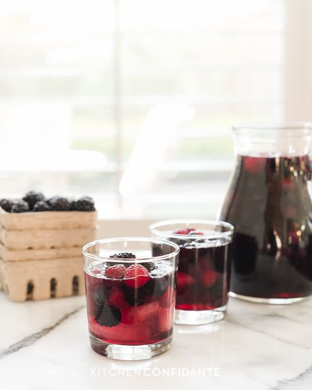 Two glasses and a pitcher of berry sangria on a countertop.