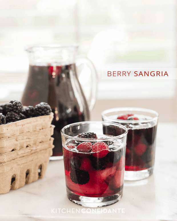 Two glasses filled with bright Berry Sangria and a pitcher with more sangria in the background.