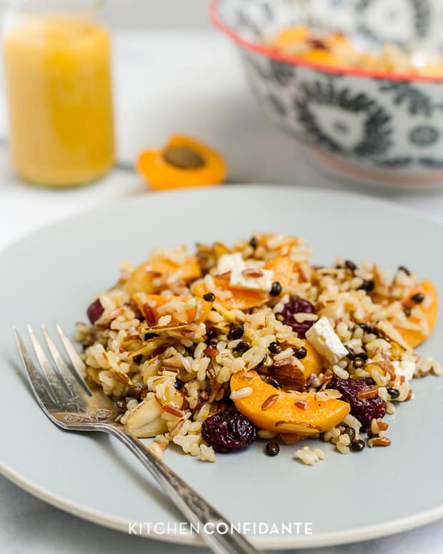 Slices of apricot tossed with cooked wild rice and dressing served on a plate.