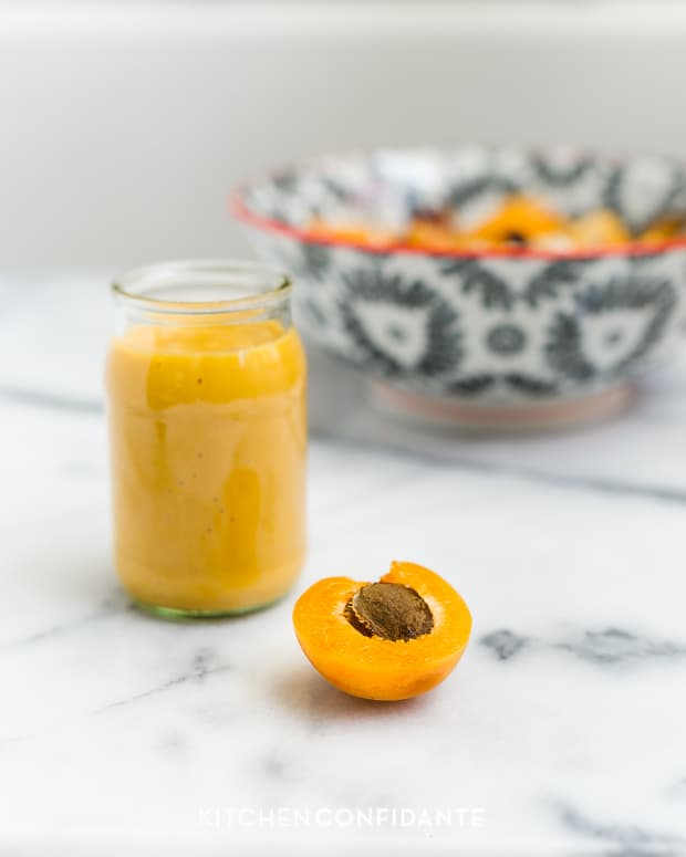A glass jar filled with apricot dressing with a half of an apricot alongside.