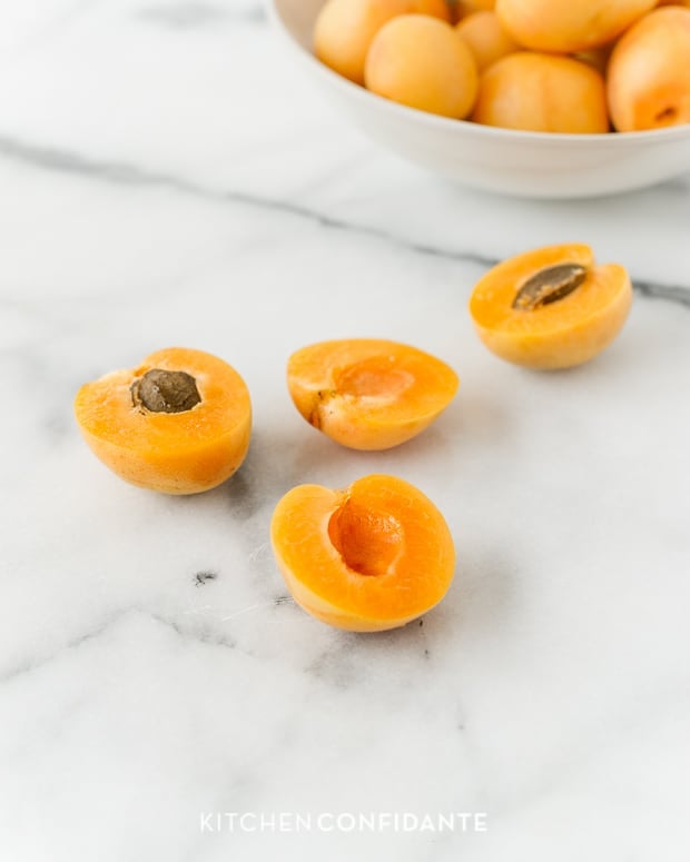 Apricots cut in half and opened on a marble surface.