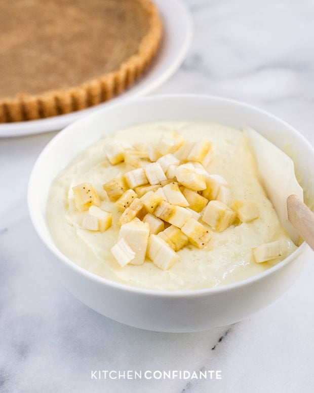 Banana cream filling in a bowl with chunks of banana being folded in with a spatula.