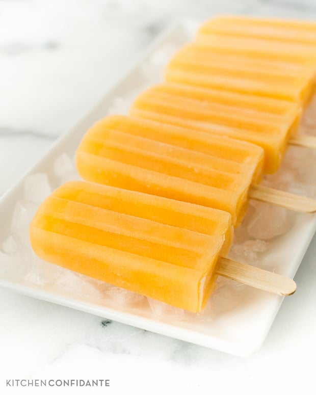 A row of Cantaloupe Lime Popsicles on an ice-covered platter.