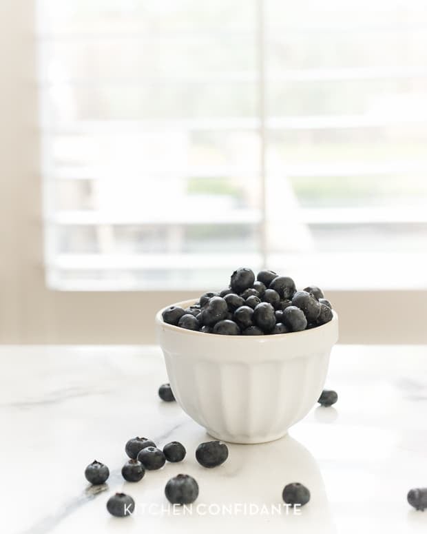 A white bowl filled with fresh blueberries on a countertop.