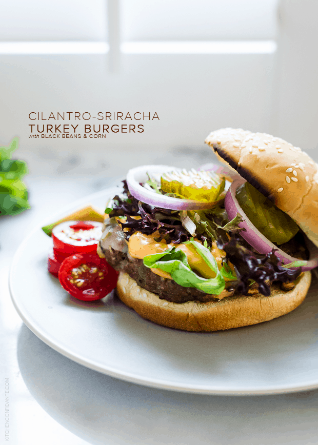 A Cilantro-Sriracha Turkey Burgers on a plate garnished with tomatoes, pickles, and onion slices.