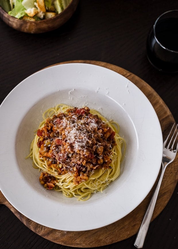 A deep white plate piled high with spaghetti and a chicken sausage and lentil bolognese and garnished with Parmesan cheese.