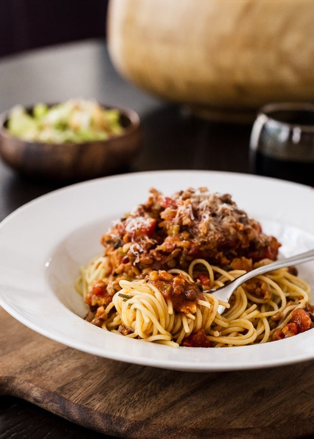 A fork swirled around a bite of spaghetti and sauce in a white dish.