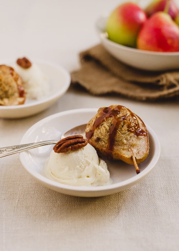 An individual Stuffed Pear Crisp served in a bowl with vanilla ice cream and a spoon. 