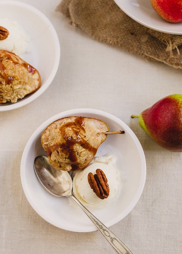 An individual Stuffed Pear Crisp served in a white bowl with a scoop of ice cream and a drizzle of caramel.