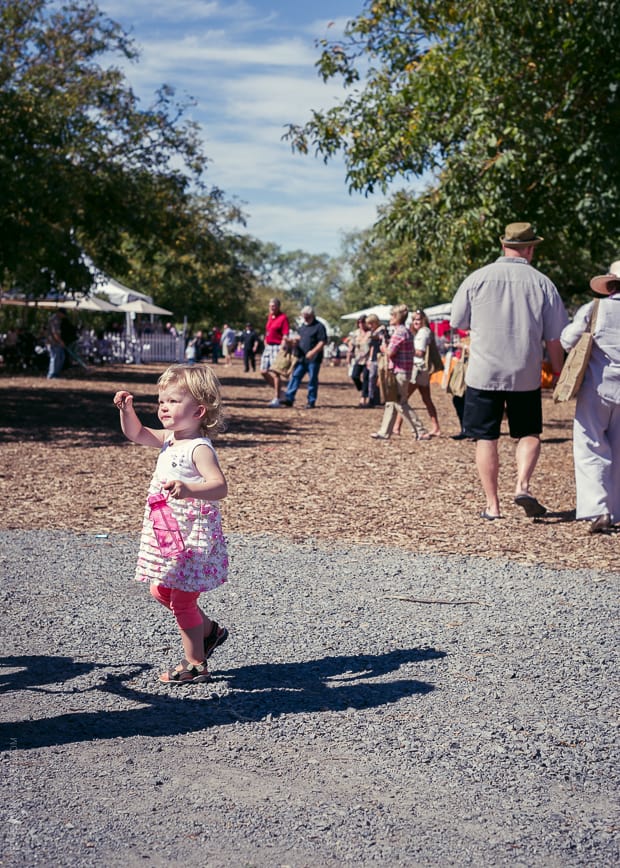 A small child walking around with her water bottle holding a tomato in her hand.