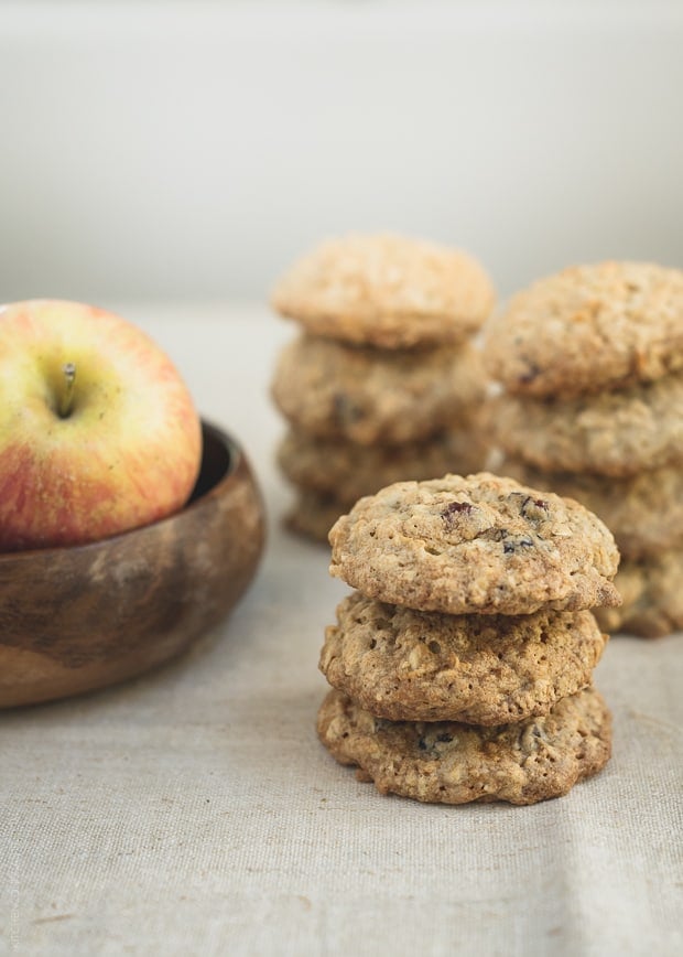 A stack of three Apple Cranberry Oatmeal Cookies surrounded by more cookies and an apple.