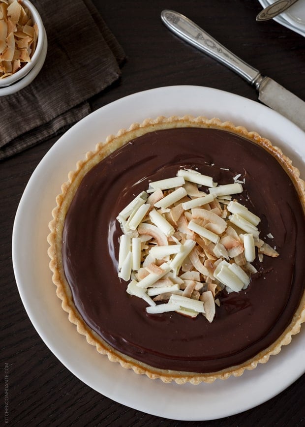 A Coconut Custard Tart with Chocolate Ganache garnished with toasted coconut and white chocolate curls.