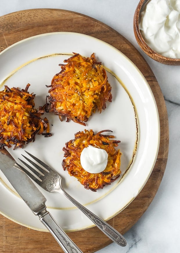 Three Sweet Potato, Turnip and Parsnip Latkes on a white plate with a fork and knife.