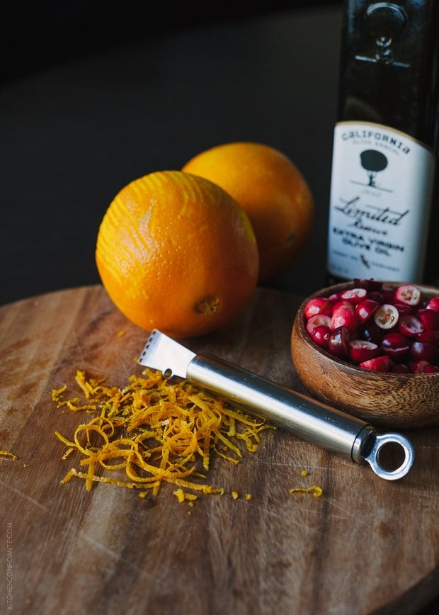 Oranges, orange zest, a zester, and a wooden bowl of cranberries.